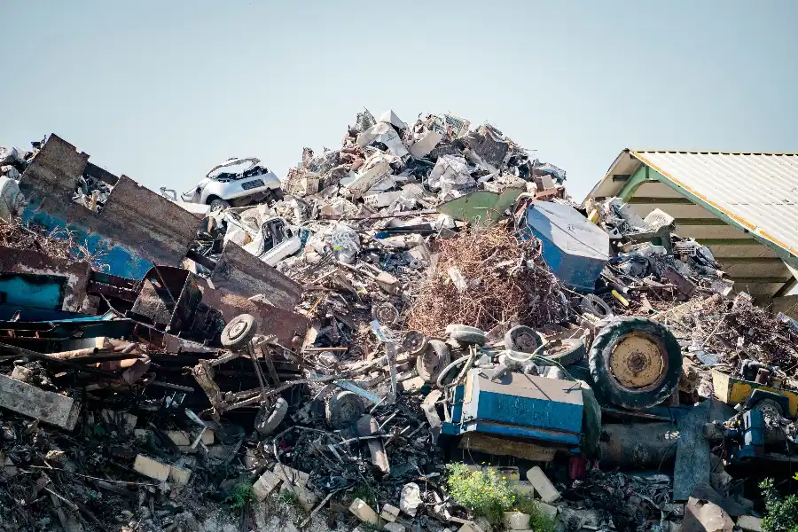 A large pile of mixed industrial scrap including crushed vehicles, metal sheets and machinery parts at an outdoor recycling yard.