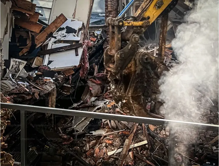 A mechanical claw tears through the bones of a crumbling building, dust rising like a final breath.