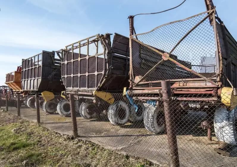 A row of weary, rust-worn trucks sitting silently behind a fence, long retired from their working days.