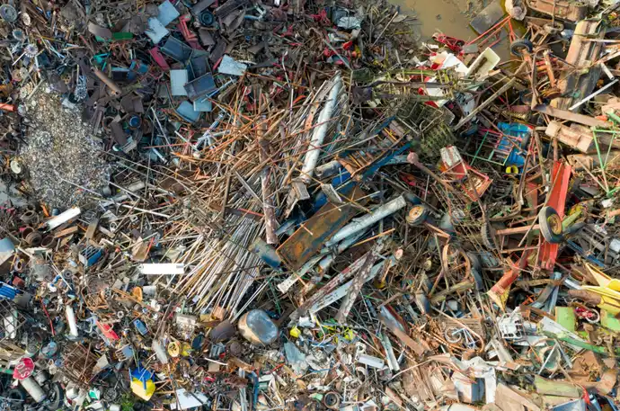 Top-down view of a large mixed scrap pile with rusted rods, old vehicles, wheels, and colourful metal debris.
