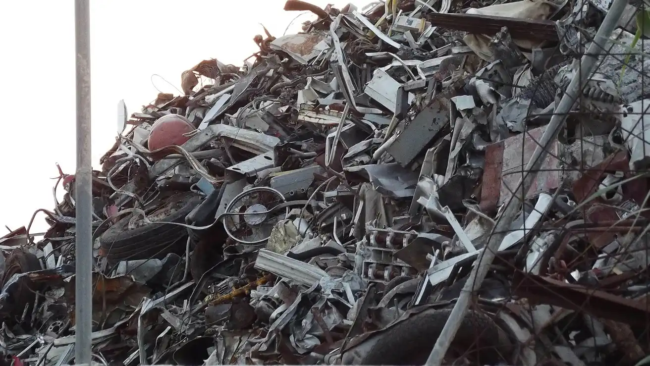 A large heap of mixed scrap metal including bike frames, sheet metal, and various metal parts piled high at a scrapyard.