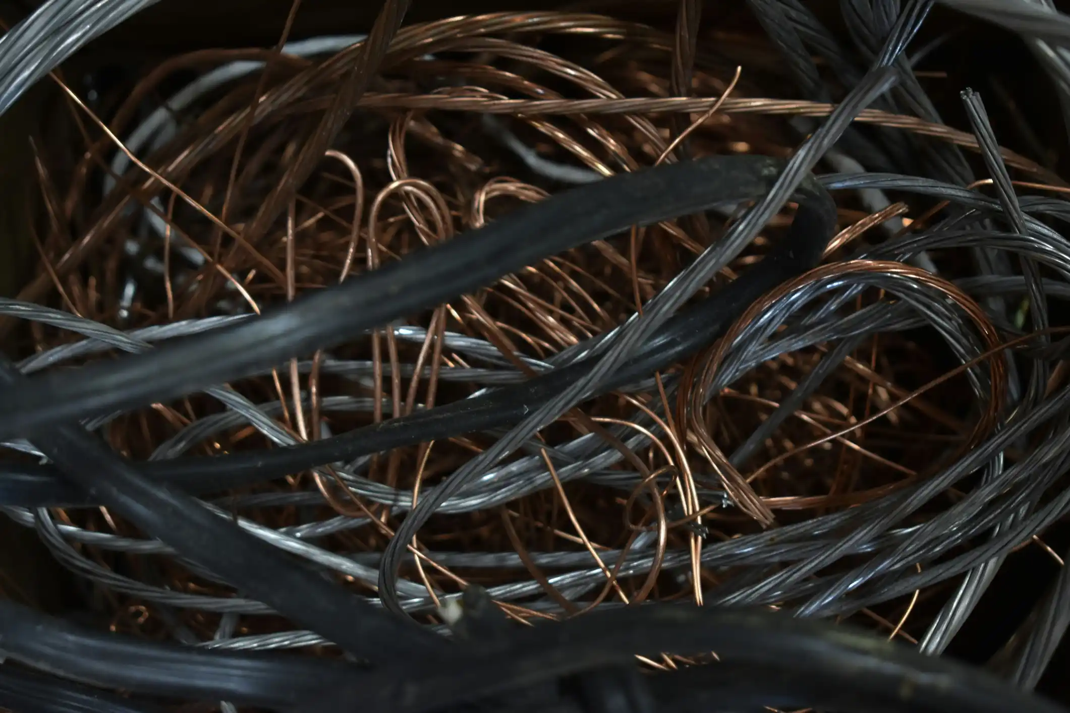 Close-up of tangled copper wire and black cables collected for scrap recycling.