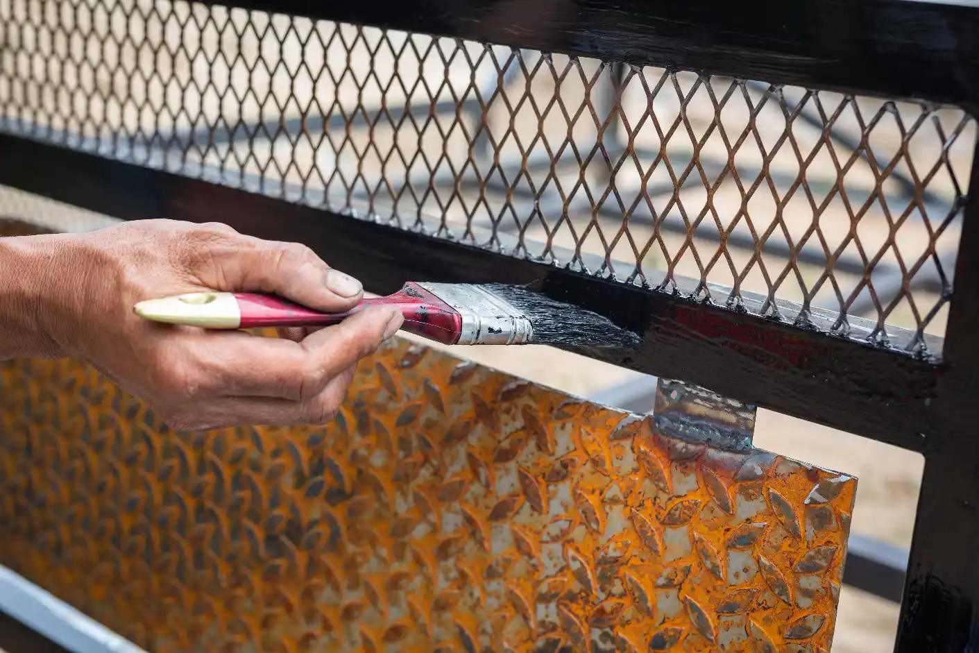 Workers preparing black steel with paint brushes before coating.