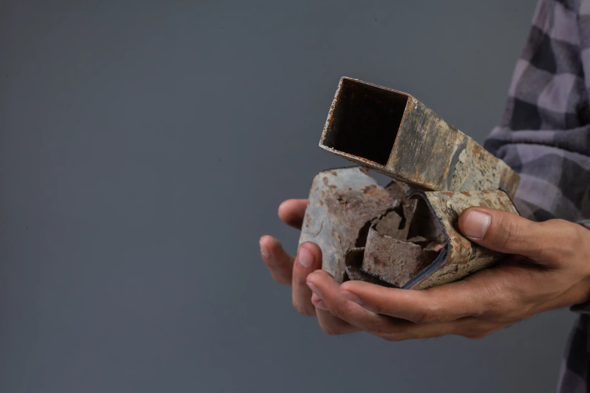 A person holding a crushed and rusted square metal tube, showing an example of recyclable scrap metal found around the home or garage.