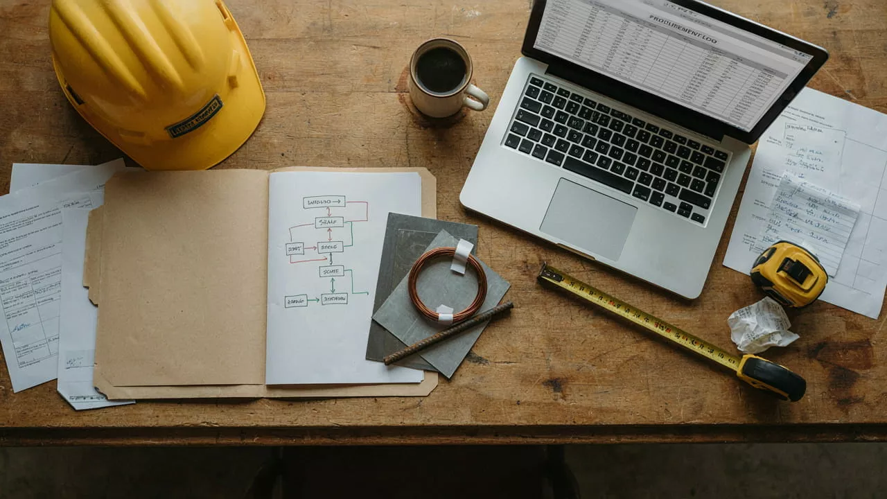 Overhead view of a job site desk with a hard hat, coffee, laptop showing a procurement log, a hand-drawn recycling workflow diagram, and samples of copper wire and sheet metal.
