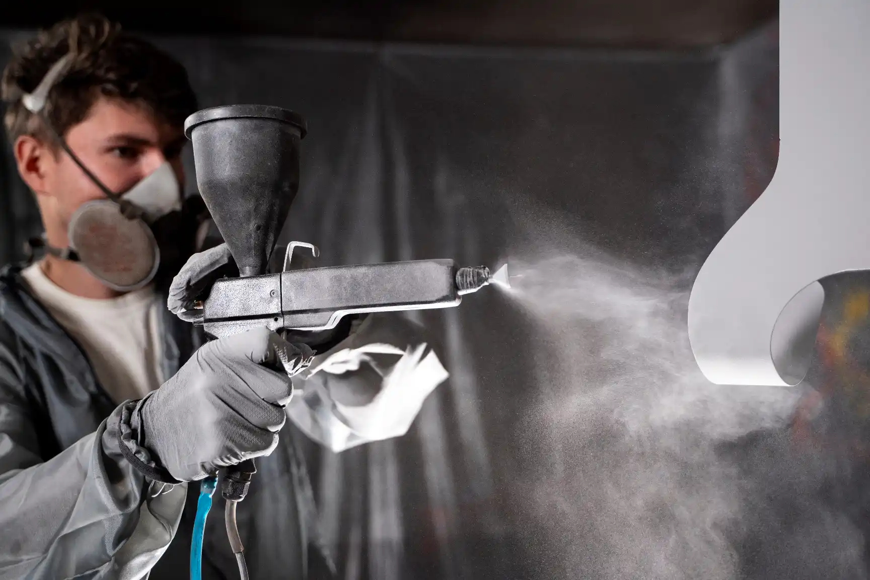 A worker applying a coating to a metal surface with a spray gun.